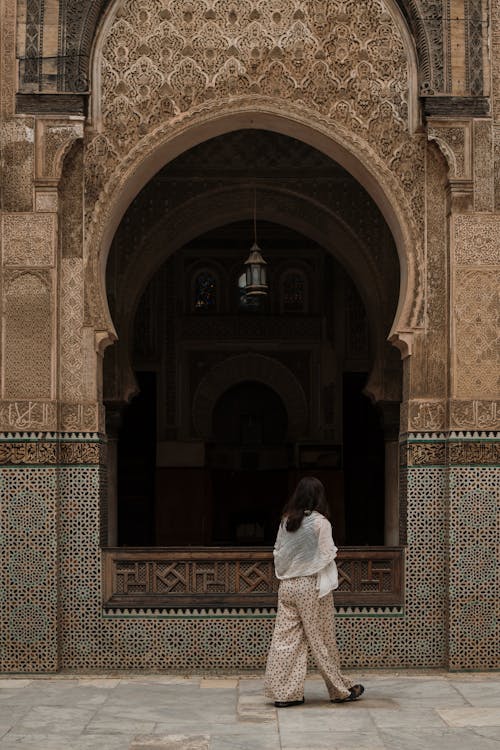 Free A woman walks by a beautifully decorated archway of a Moroccan mosque in Fes, showcasing traditional Islamic architecture. Stock Photo