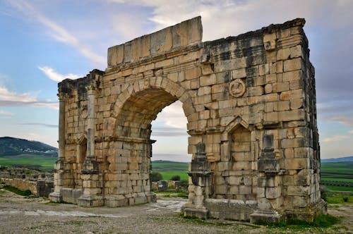 Free Stunning view of the ancient Roman arch in Volubilis, Morocco amid a serene landscape. Stock Photo