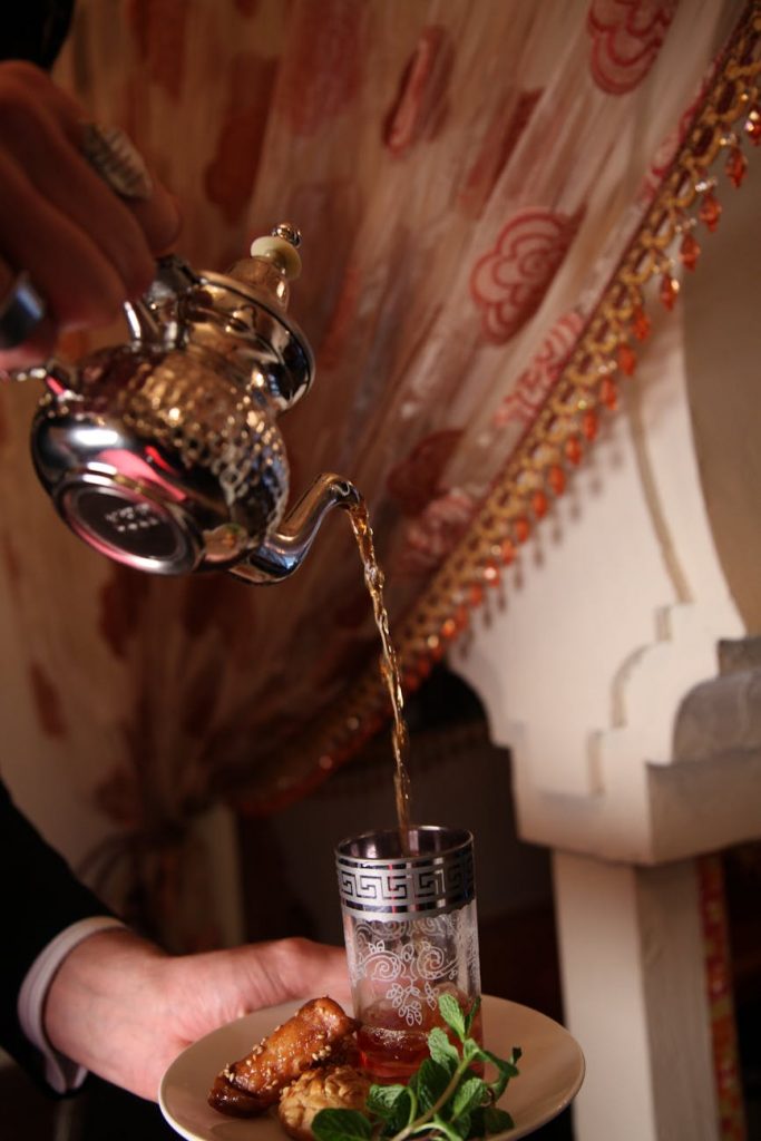 person pouring tea cup glass near brown curtain