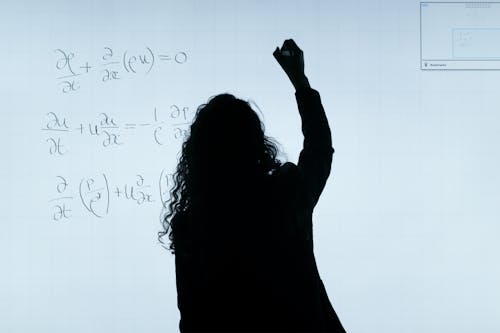 Free A silhouette of a woman writing mathematical equations on a large whiteboard, representing education and analysis. Stock Photo