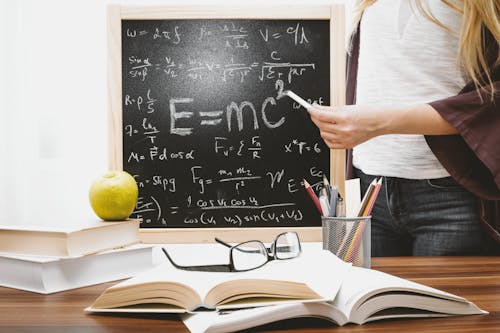 Free Moroccan Woman writing physics equations on a blackboard with books and an apple on the desk. Stock Photo