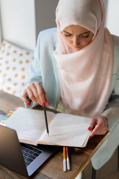 Free Middle Eastern woman in hijab studying with laptop and notepad indoors. Stock Photo