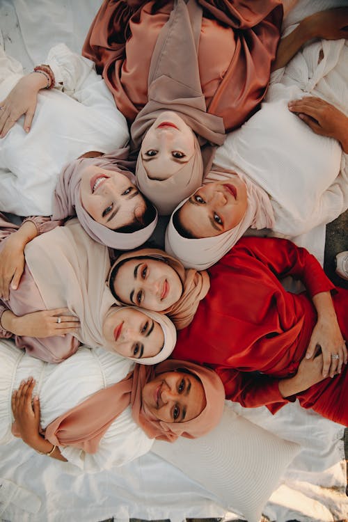 Free Aerial view of diverse women in hijabs lying on a blanket outdoors, embracing each other. Stock Photo