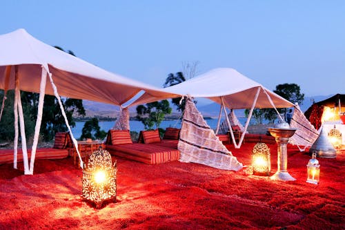 Free Traditional Moroccan tent setup with lanterns by the lakeside at twilight in Ouarzazate. Stock Photo
