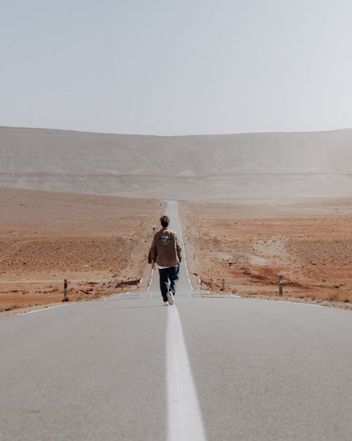 Free A lone traveler walks down an endless road in the Moroccan desert landscape. Stock Photo