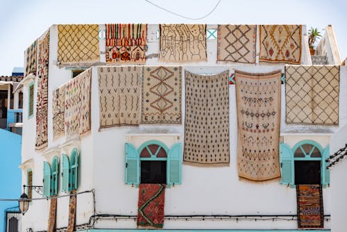 Free Traditional Moroccan rugs hanging on a white building's facade under bright daylight. Stock Photo
