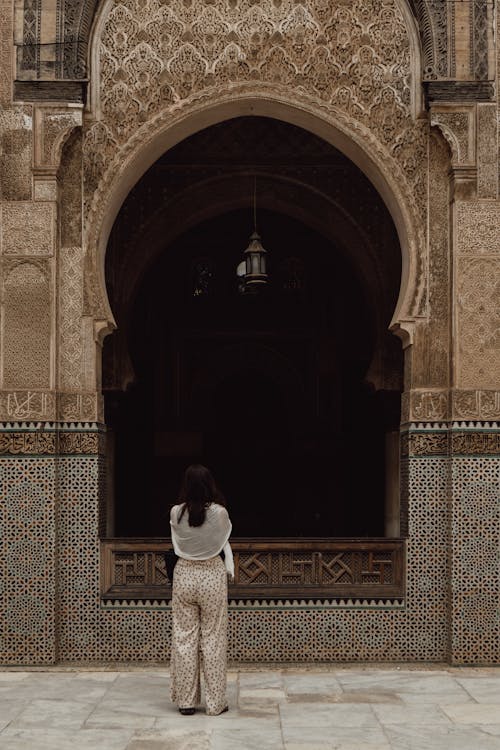Free A woman stands in front of a beautifully intricate mosque arch in Fes, Morocco. Stock Photo