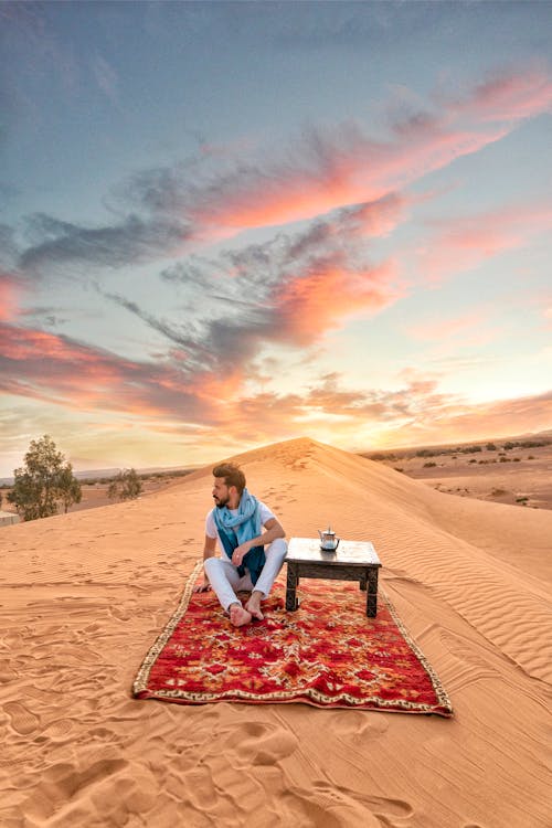 Free Serene image of a person relaxing on a carpet in the Moroccan desert at sunrise. Stock Photo