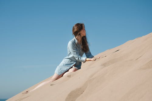 Free Woman in casual attire climbing sand dunes under a clear blue sky in Morocco. Stock Photo