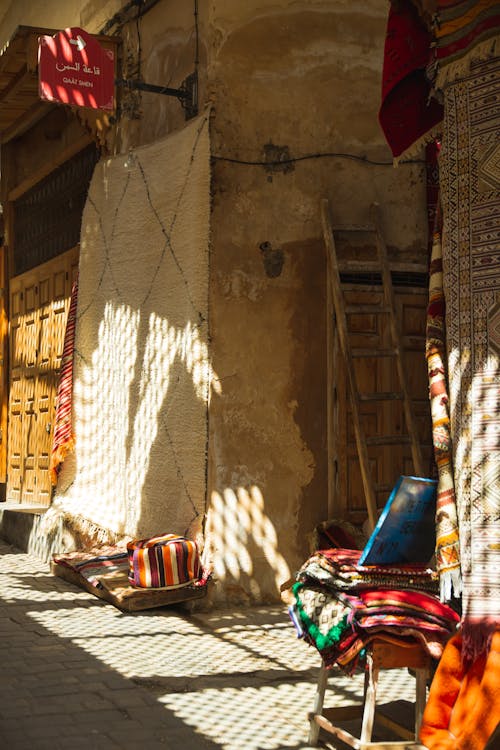 Free Sunlit Moroccan street with colorful textiles and rustic charm in Fes. Stock Photo