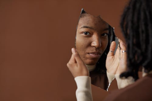Free A woman holding and looking into a broken mirror, reflecting on self image and identity. Stock Photo