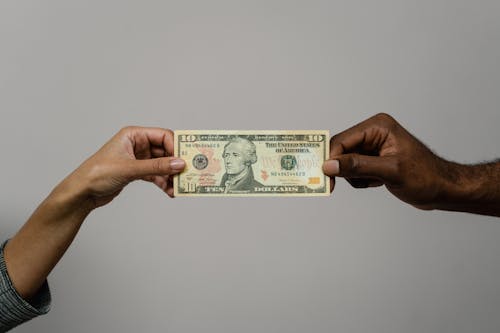Free Close-up of two hands exchanging a ten dollar bill, symbolizing financial transaction or exchange. Stock Photo