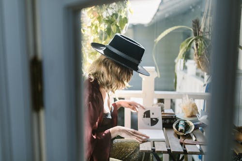 Free A woman in a hat reading tarot cards on a sunlit balcony surrounded by crystals. Stock Photo