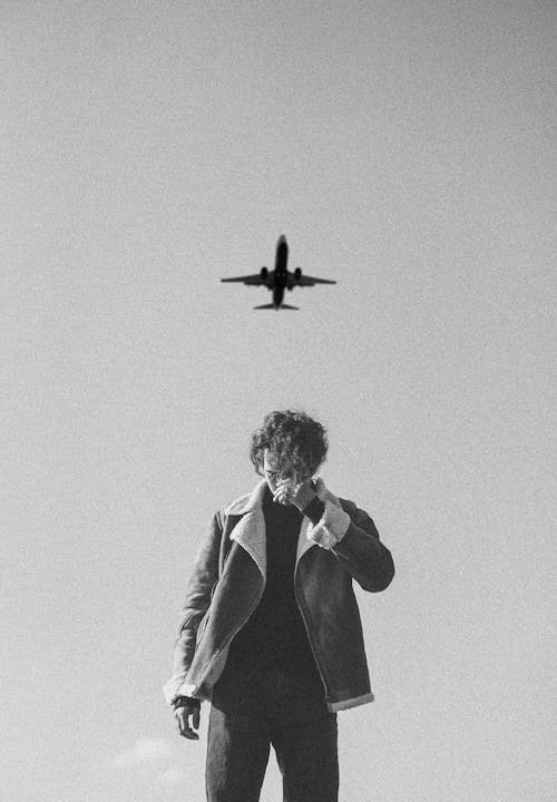 Free Black and white photo of a man outdoors under a flying airplane. Stock Photo