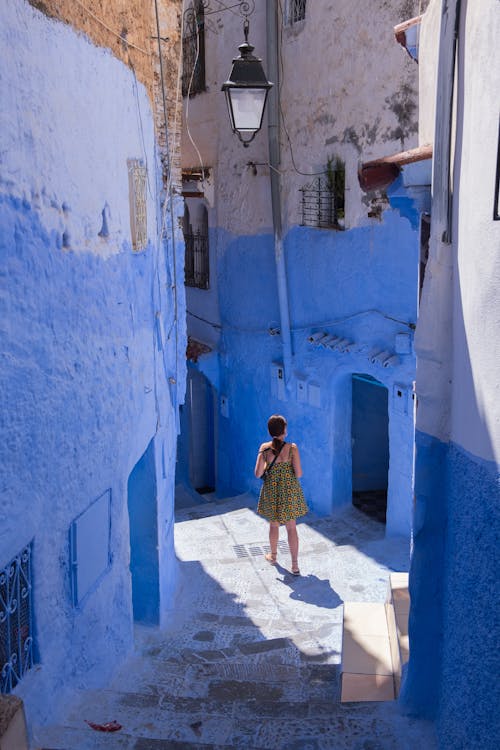 Free A woman strolls through a vibrant blue-painted alleyway on a sunny day, capturing cultural architecture. Stock Photo