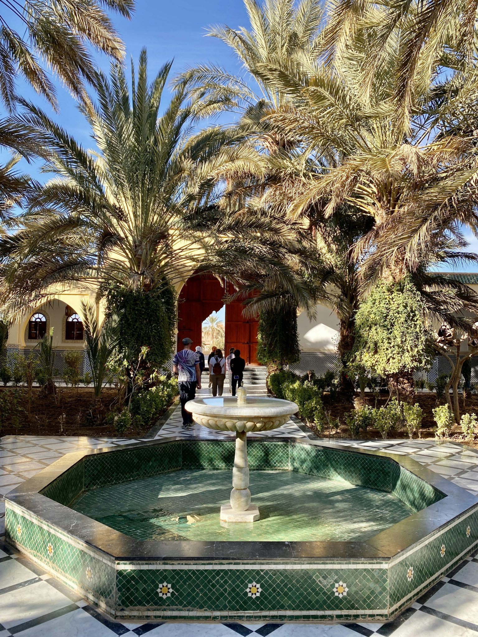 a fountain surrounded by palm trees in front of a building