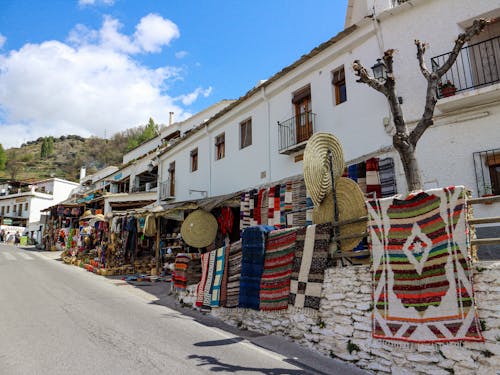 Free Vibrant handmade rugs and souvenirs at an outdoor street market with whitewashed buildings. Stock Photo